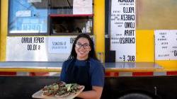 年轻的西班牙裔女子站在餐车前端着一盘墨西哥卷饼